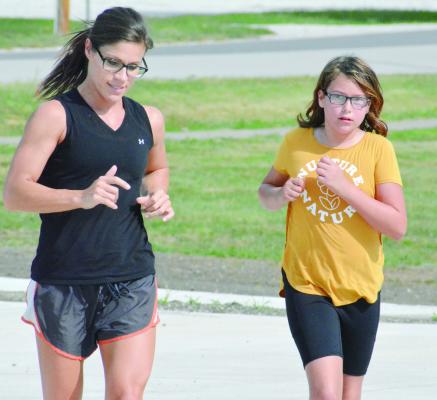 FIRST-YEAR Hardin-Central cross country coach Jenni Scott, left, trains with her athletes. They include sixth-grader Tayler Mead, who finishes a run with her Sept. 1 at the school campus. SHAWN RONEY | Staff