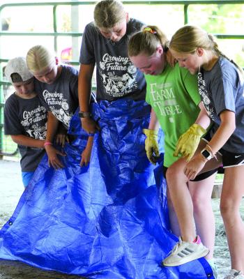 WALKER WILLIAMS (from left), Hazel Dorton, Sophia Dorton, Audrey Covery and Jojo Williams work together to flip a tarp completely over without stepping off during a team competition.
