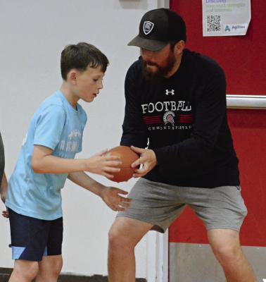ISAIAH DALLE (left) takes a handoff from Richmond assistant varsity football coach Michael Lee after a youth football camp is forced indoors because of inclement weather. SHAWN RONEY | Staff