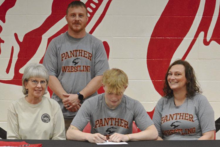 SENIOR CAYDEN MORRIS signs his letter of intent April 22 in the Richmond High School gym to study and wrestle at Neosho County Community College in Chanute, Kan. He is flanked by his grandmother, Jill Jennings (left); and mother, Nyna Anderson. His coach, Cody Hogan, stands behind him. SHAWN RONEY | Staff