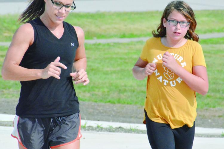 FIRST-YEAR Hardin-Central cross country coach Jenni Scott, left, trains with her athletes. They include sixth-grader Tayler Mead, who finishes a run with her Sept. 1 at the school campus. SHAWN RONEY | Staff