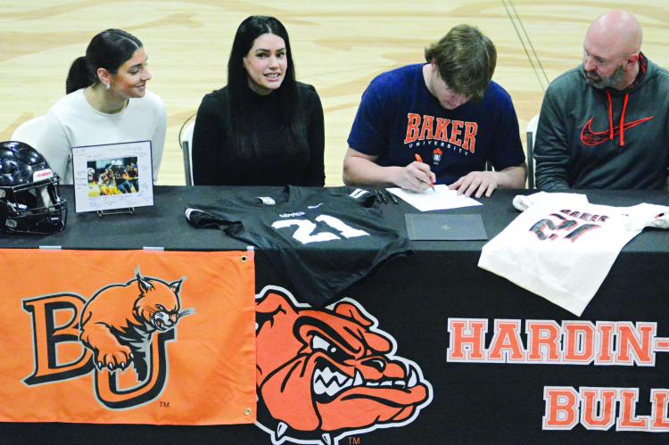 SPORTING HIS Baker University T-shirt, Hardin-Central senior Gage Smith signs his letter of intent to play college football. Also pictured amid the memorabilia are (from left) Mackenzie Smith, Marie Smith and Travis Smith. SHAWN RONEY | Staff