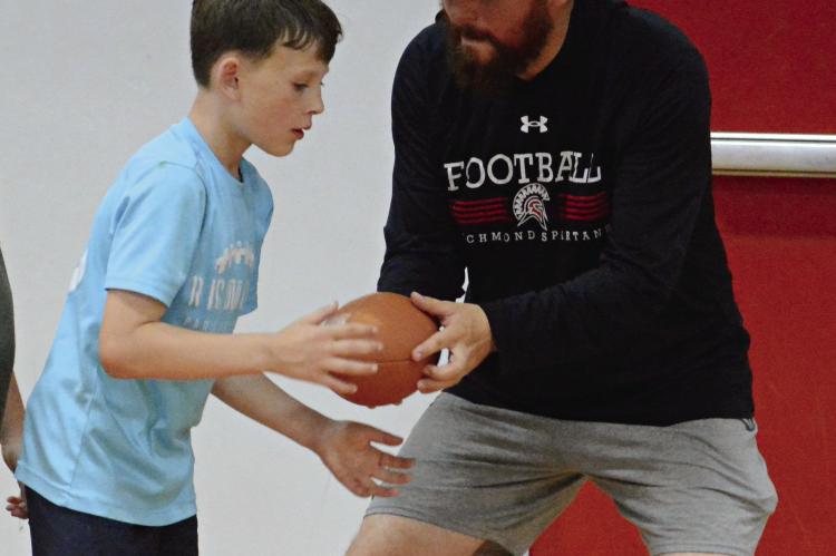 ISAIAH DALLE (left) takes a handoff from Richmond assistant varsity football coach Michael Lee after a youth football camp is forced indoors because of inclement weather. SHAWN RONEY | Staff