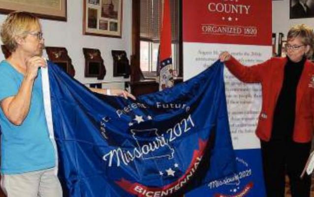 RAY COUNTY Clerk Glenda Powell, left, and Rep. Peggy McGaugh unfurl the state bicentennial celebration flag.