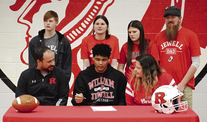 RICHMOND SENIOR Hayden Happy (center) signs his letter of intent recently in the RHS gym to play football and study at William Jewell College. Others pictured are (from left), front row, Nick Persell and Roxann Happy; second row, Georgan Happy, Evie Happy, Oli Happy and Chris Happy. SHAWN RONEY | Staff