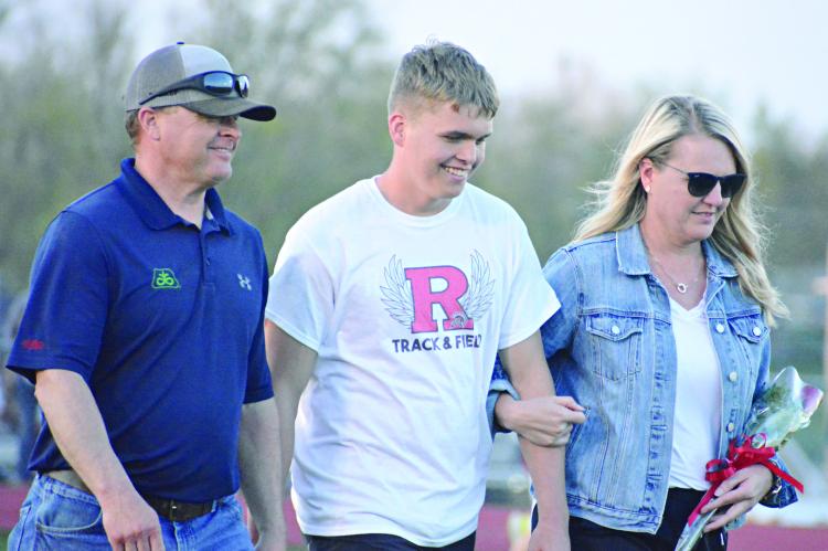 ELI STEELE smiles as he’s escorted near the end of the Hoot Middleton Invitational Tuesday at Spartan Stadium by his parents, Brian and Melissa Steele, to help commemorate Senior Night. SHAWN RONEY | Staff