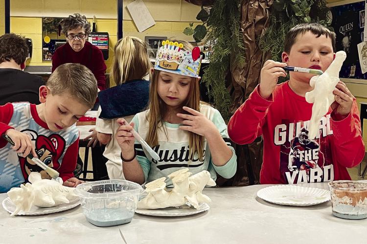 COOPER TRINDLE, ASPEN WEIR and Bentley Stephens glaze the clay dinosaurs they’re creating at Dear Elementary Clay Night. Each takes direction from Dear art teacher Bea Hendrix, who explains how to get coverage. See page 2 for the story. SOPHIA BALES | Staff