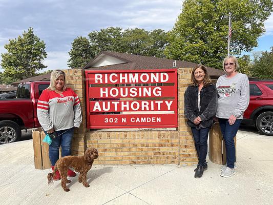 APRIL MAULSBY; Cali, the office pup; Valerie MacDonald; and Helen Sinderson are standing in front of a sign that the Housing Authority’s maintenance department homecrafted themselves. Maulsby says she and her team are impressed by the rating and effort that has been put into it. SOPHIA BALES | Staff