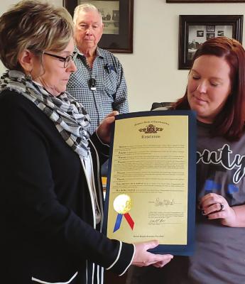 A SERVANT REMEMBERED: Missouri State Rep. Peggy McGaugh presents Melissa Perkins a House resolution. The document recognizes the service of Perkins’ husband, the late Jeffrey “Jeff” Cole Perkins, a Ray County Sheriff’s Office sergeant. From left, front, are McGaugh and Perkins. Behind them is Commissioner Jerry Bishop. JANIS KINCAID | Submission