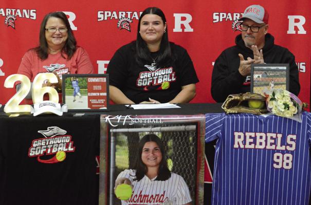 FLANKED BY family members and amid her softball memorabilia, Richmond senior Elizabeth beams during her signing ceremony. Also pictured are her parents, Heather (from left) and Shannon Wood. SHAWN RONEY | Staff