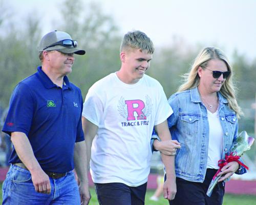 ELI STEELE smiles as he’s escorted near the end of the Hoot Middleton Invitational Tuesday at Spartan Stadium by his parents, Brian and Melissa Steele, to help commemorate Senior Night. SHAWN RONEY | Staff