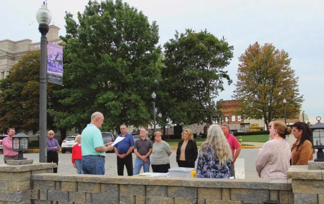 STANDING ACROSS from the Ray County Courthouse in front of the city park being built at West North Main and North College streets, Ray County Bicentennial Committee member Dr. Hal Middleton reads from a paper telling the community leaders standing in front of him on the sidewalk what will go into the time capsule. J.C. VENTIMIGLIA | Staff