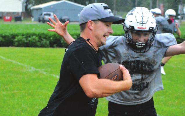 AS THE RAIN FALLS, Norborne Hardin-Central assistant coach Zac Smith carries the football to help Aggies like Kalel Bowman work on defensive pursuit Monday morning on one of the practice fields at Hardin-Central. SHAWN RONEY | Staff