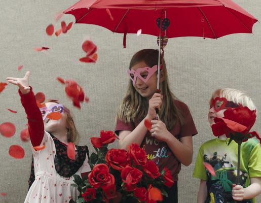 BLAKE BUCKMAN (from left) joins Ryann and Ries Madget in a shower of rose petals during “Valentine Fun: Secrets, Surprises, and Sweet History” hosted by Sarah Poff at the Ray County Library. SHARON DONAT | Staff
