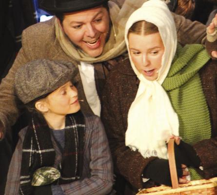 THE CRATCHIT FAMILY sings while they shop at the open air market before Christmas day. Tiny Tim (from left) Bob Cratchit, and Ethal Cratchit, were played by Paige Quick, Ryan Kugler and Annie Quick, respectively. SHARON DONAT | Staff