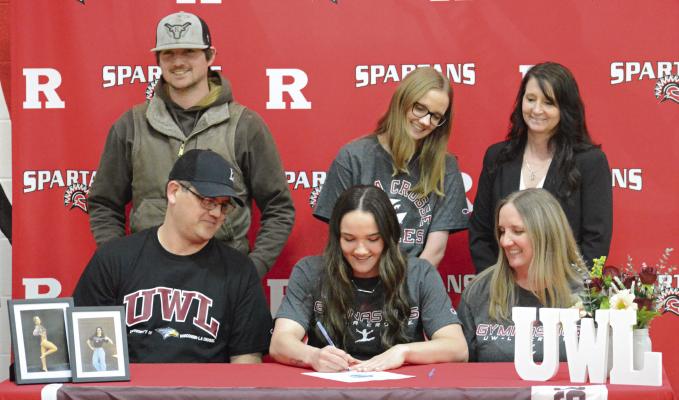 COBI POWELL (front, center) signs her letter of intent to compete in gymnastics at the University of Wisconsin-La Crosse. Watching are her parents Brian and Brandi Powell (front row, from left) and back row, brother Dylan Powell, sister Ali Powell and former coach Mandi Saur. Look for additional coverage April 18. SHAWN RONEY | Staff