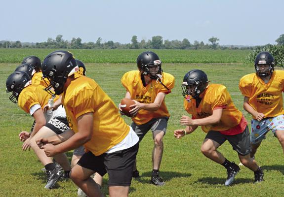 WITH THE BALL firmly clasped in both hands, Bearcats quarterback Jonathon Harris looks to hand off as his linemen rise up to block near the end of Orrick’s June 16 8-man football camp session on the Orrick practice field. SHAWN RONEY | Staff
