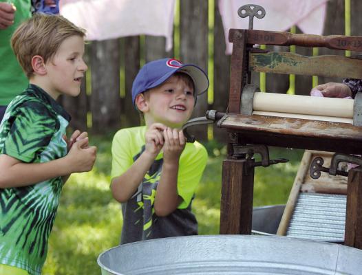 GRIFFON (LEFT) AND Kylan Sloop help feed laundry through a vintage wringer washer.