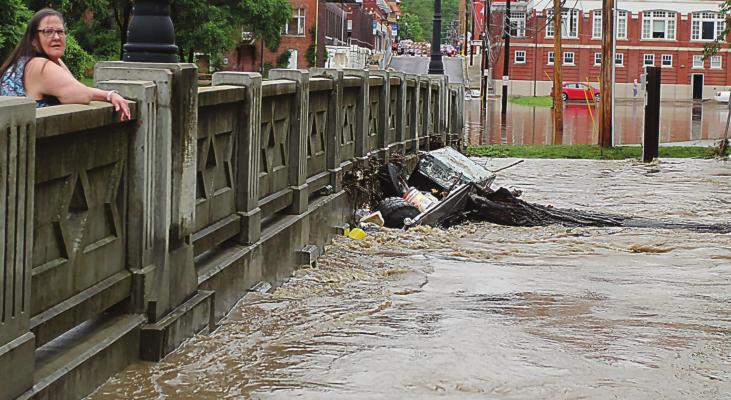 A COMMUNITY VISITOR, Melanie Cantwell, Springfield, stands on the Marietta Street Bridge while watching flash flood water from the Fishing River slap against the bridge bottom June 25, 2021. J.C. VENTIMIGLIA | Staff