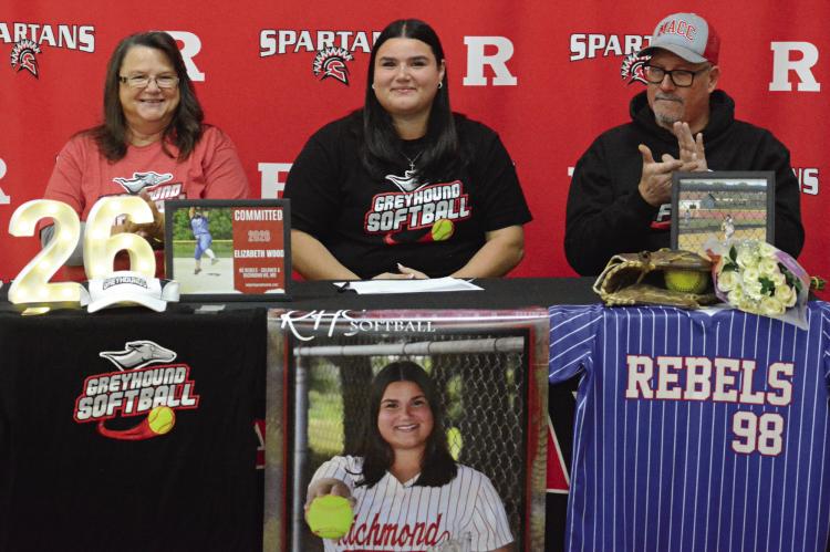 FLANKED BY family members and amid her softball memorabilia, Richmond senior Elizabeth beams during her signing ceremony. Also pictured are her parents, Heather (from left) and Shannon Wood. SHAWN RONEY | Staff