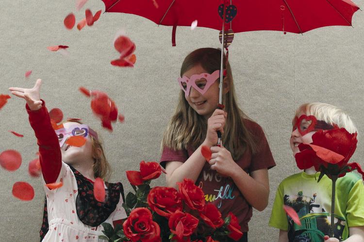 BLAKE BUCKMAN (from left) joins Ryann and Ries Madget in a shower of rose petals during “Valentine Fun: Secrets, Surprises, and Sweet History” hosted by Sarah Poff at the Ray County Library. SHARON DONAT | Staff