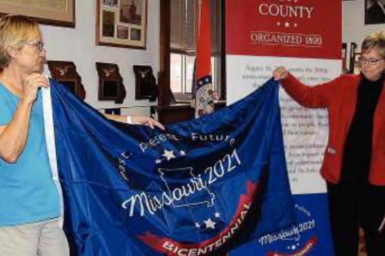 RAY COUNTY Clerk Glenda Powell, left, and Rep. Peggy McGaugh unfurl the state bicentennial celebration flag.