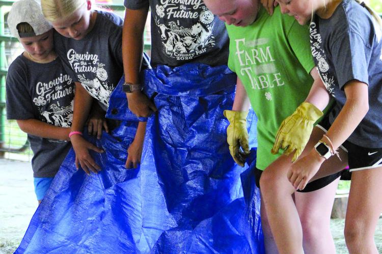 WALKER WILLIAMS (from left), Hazel Dorton, Sophia Dorton, Audrey Covery and Jojo Williams work together to flip a tarp completely over without stepping off during a team competition.