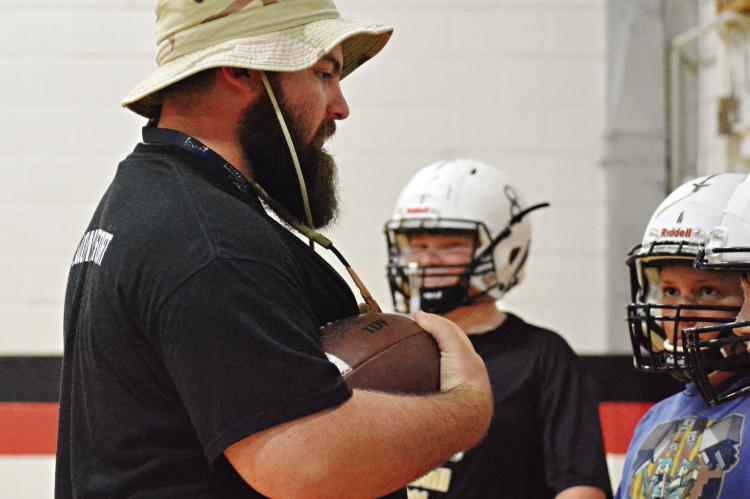 WITH THE pigskin tucked in his arm, Norborne Hardin-Central junior high coach Tommy Burton teaches his young Aggies about ball security during 8-man football team camp Monday morning in the Hardin-Central gym. SHAWN RONEY | Staff