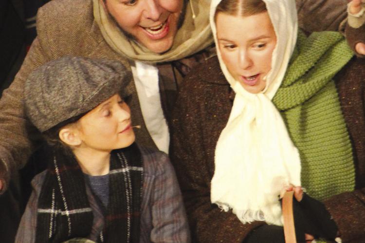 THE CRATCHIT FAMILY sings while they shop at the open air market before Christmas day. Tiny Tim (from left) Bob Cratchit, and Ethal Cratchit, were played by Paige Quick, Ryan Kugler and Annie Quick, respectively. SHARON DONAT | Staff