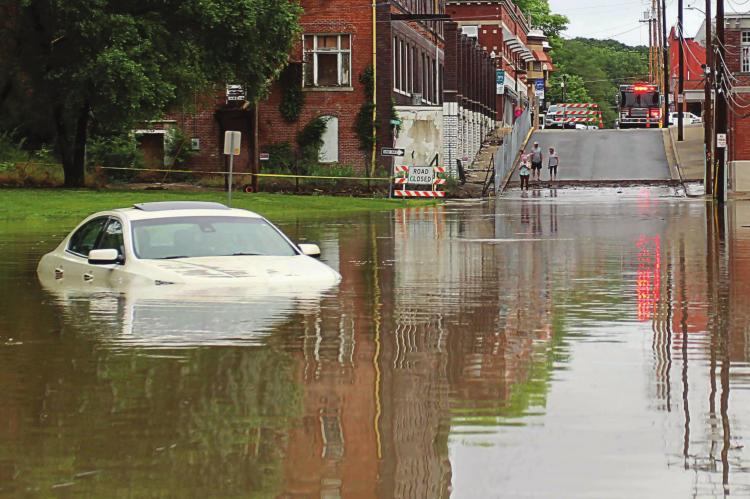 AS SEEN from the South Marietta Street Bridge in downtown Excelsior Springs, flood water spills out from the Fishing River and covers the north side of the street, where this Lincoln remains surrounded after the driver is rescued around 6 a.m. June 24 by city emergency personnel. Flood water inundates lots that would have been used for WaterFest parking and traps vehicles already parked there. J.C. VENTIMIGLIA | Staff