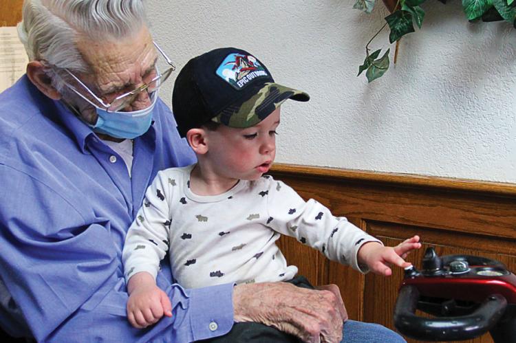 AFTER WAITING for a year, Bill Graff, 90, gets to hold great grandson Von Graff, 1, who presses the scooter’s beeper. Bill is glad for the visit from his family: “Good Lord, it makes life worth living. You betcha.”