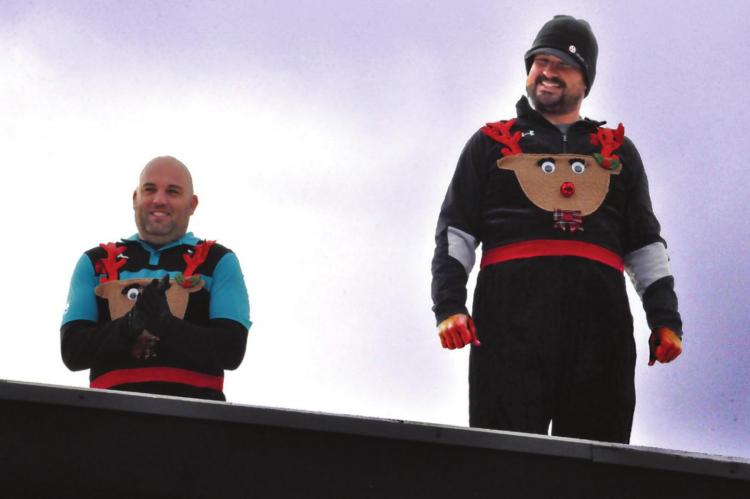 DONNING Christmas outfits, Richmond varsity boys basketball coach Kevin Jermain, left, and varsity football coach Nick Persell stand on the roof Monday at Richmond High School. Jermain, Persell, varsity girls basketball coach Chad Snyder, Athletic Director Matt Habermehl and Principal Brandon Quick spend the night on the roof.
