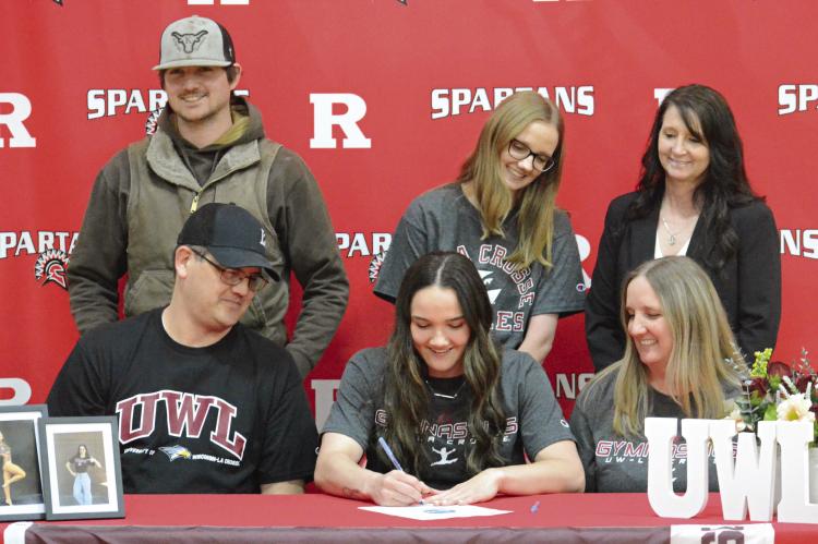 COBI POWELL (front, center) signs her letter of intent to compete in gymnastics at the University of Wisconsin-La Crosse. Watching are her parents Brian and Brandi Powell (front row, from left) and back row, brother Dylan Powell, sister Ali Powell and former coach Mandi Saur. Look for additional coverage April 18. SHAWN RONEY | Staff