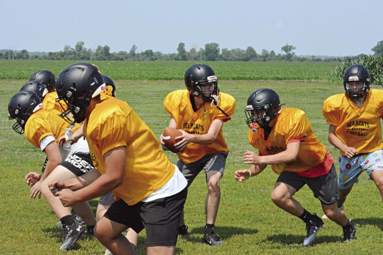 WITH THE BALL firmly clasped in both hands, Bearcats quarterback Jonathon Harris looks to hand off as his linemen rise up to block near the end of Orrick’s June 16 8-man football camp session on the Orrick practice field. SHAWN RONEY | Staff