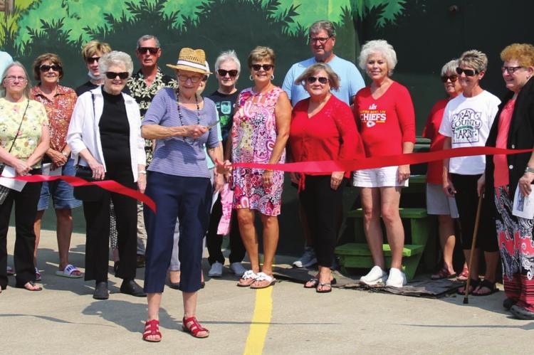 RAY COUNTY artist Patricia Pierce, who did the sketch that led to the mural, cuts the ribbon to dedicate the work of art officially in downtown Richmond.