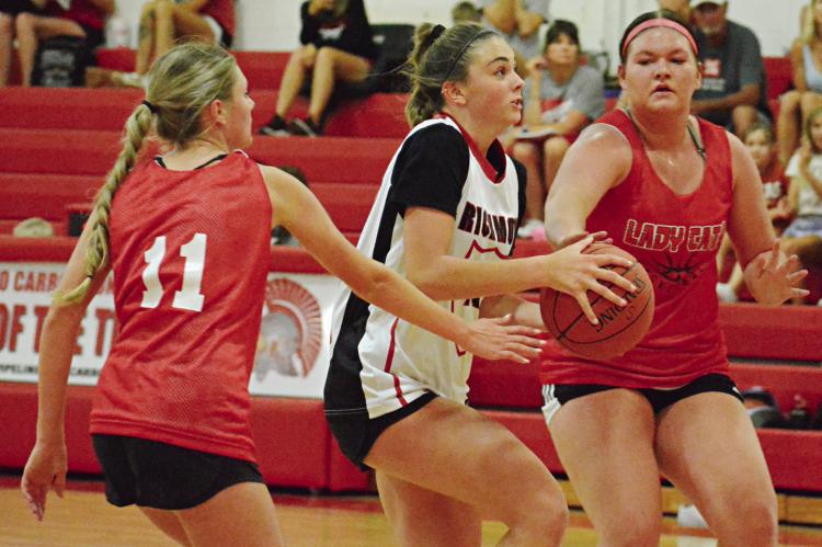 WITH THE BASKETBALL in both hands, Richmond’s Emma Hash looks to split through two Braymer defenders Monday in River Valley Shootout action at Carrollton. SHAWN RONEY | Staff
