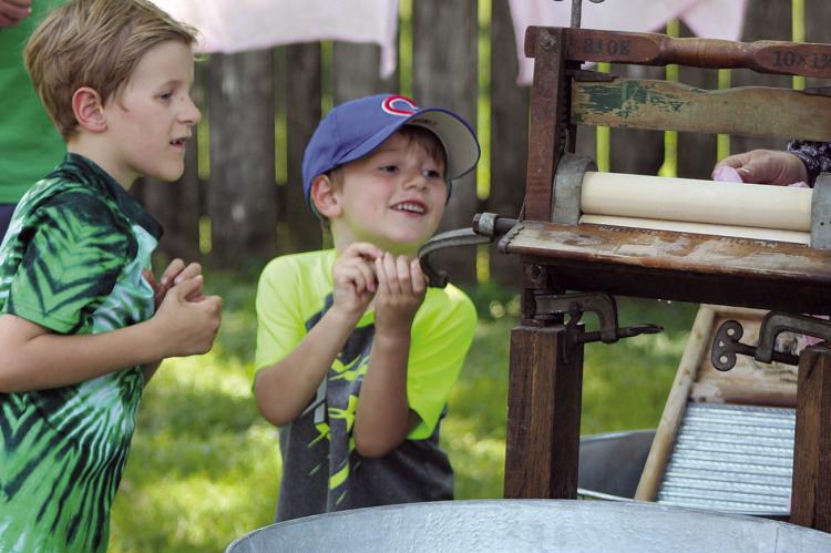GRIFFON (LEFT) AND Kylan Sloop help feed laundry through a vintage wringer washer.