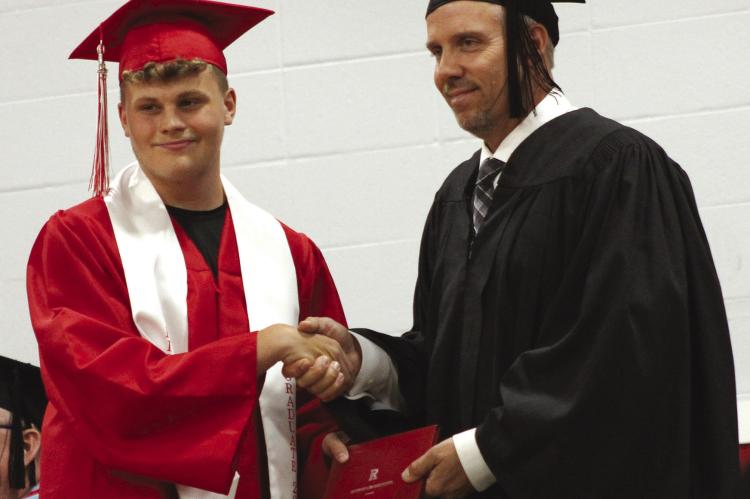 ETHAN HALL (left) shakes hands with Board of Education President Jon Dana during the commencement.