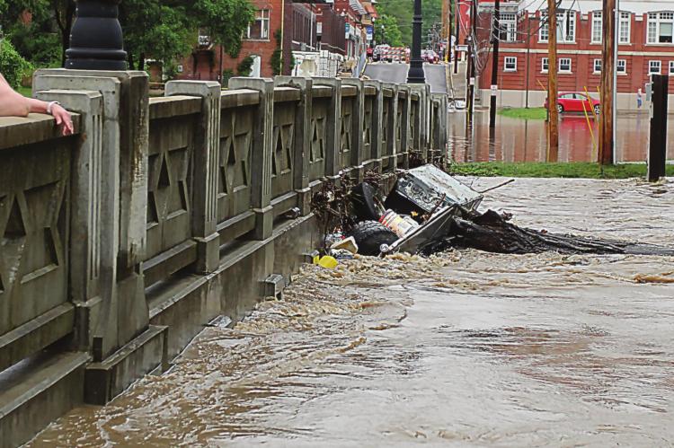 A COMMUNITY VISITOR, Melanie Cantwell, Springfield, stands on the Marietta Street Bridge while watching flash flood water from the Fishing River slap against the bridge bottom June 25, 2021. J.C. VENTIMIGLIA | Staff