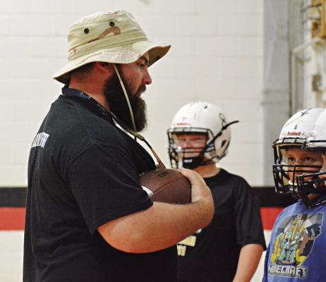 WITH THE pigskin tucked in his arm, Norborne Hardin-Central junior high coach Tommy Burton teaches his young Aggies about ball security during 8-man football team camp Monday morning in the Hardin-Central gym. SHAWN RONEY | Staff
