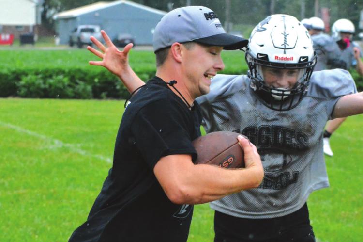 AS THE RAIN FALLS, Norborne Hardin-Central assistant coach Zac Smith carries the football to help Aggies like Kalel Bowman work on defensive pursuit Monday morning on one of the practice fields at Hardin-Central. SHAWN RONEY | Staff