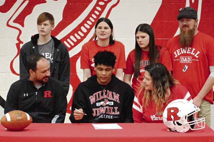 RICHMOND SENIOR Hayden Happy (center) signs his letter of intent recently in the RHS gym to play football and study at William Jewell College. Others pictured are (from left), front row, Nick Persell and Roxann Happy; second row, Georgan Happy, Evie Happy, Oli Happy and Chris Happy. SHAWN RONEY | Staff