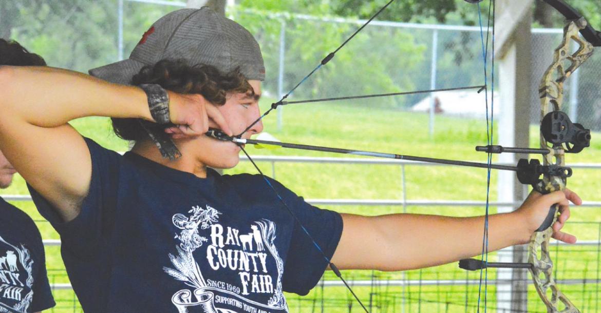 WITH BIG BROTHER Blake behind him, Trent Logsdon takes aim during the archery competition Saturday, July 16 at the Ray County Fair in Richmond. Shawn Roney | Staff